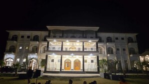 A large, multi-story building with a symmetrical facade, multiple balconies, and a central entrance with a wooden door. - Evergreen Resort And SPA  The Lychee  (Kaladhungi)