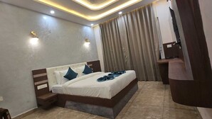 A modern hotel room with a large bed, a nightstand, and a built-in desk. - Evergreen Resort And SPA  The Lychee  (Kaladhungi)