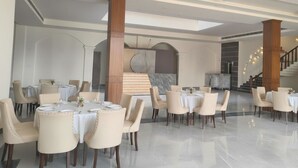 A spacious dining area with round tables and chairs, a marble column, and a staircase in the background. - Evergreen Resort And SPA  The Lychee  (Kaladhungi)