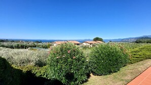 Una villa con jardín, vistas al mar y un paisaje montañoso al fondo.