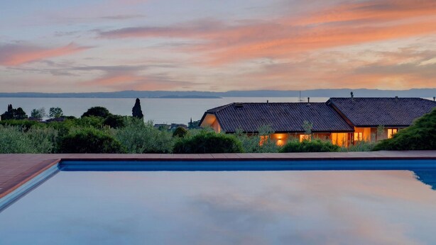 Una piscina con vistas a una casa y una masa de agua durante la puesta de sol.