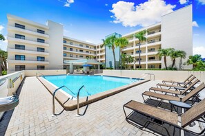 A hotel pool area with a rectangular pool, lounge chairs, and a covered seating area. - Gulf & Bay Club - F306 (Siesta Key)