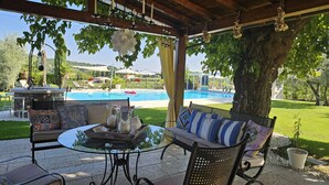 Un patio al aire libre con una mesa de vidrio, sillas de mimbre y un sofá. Se ve una piscina al fondo.