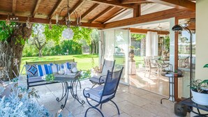 Un patio techado con techo de madera, una puerta de vidrio que da al exterior, y una mesa con sillas.