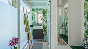 A narrow hallway with a bathroom featuring a sink, mirror, and green patterned wallpaper.