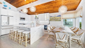 Una cocina moderna con armarios blancos, una isla de mármol y una zona de comedor con sillas de mimbre.