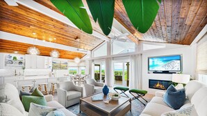 Amplia sala de estar con techo de madera, chimenea, televisor y vistas al exterior.
