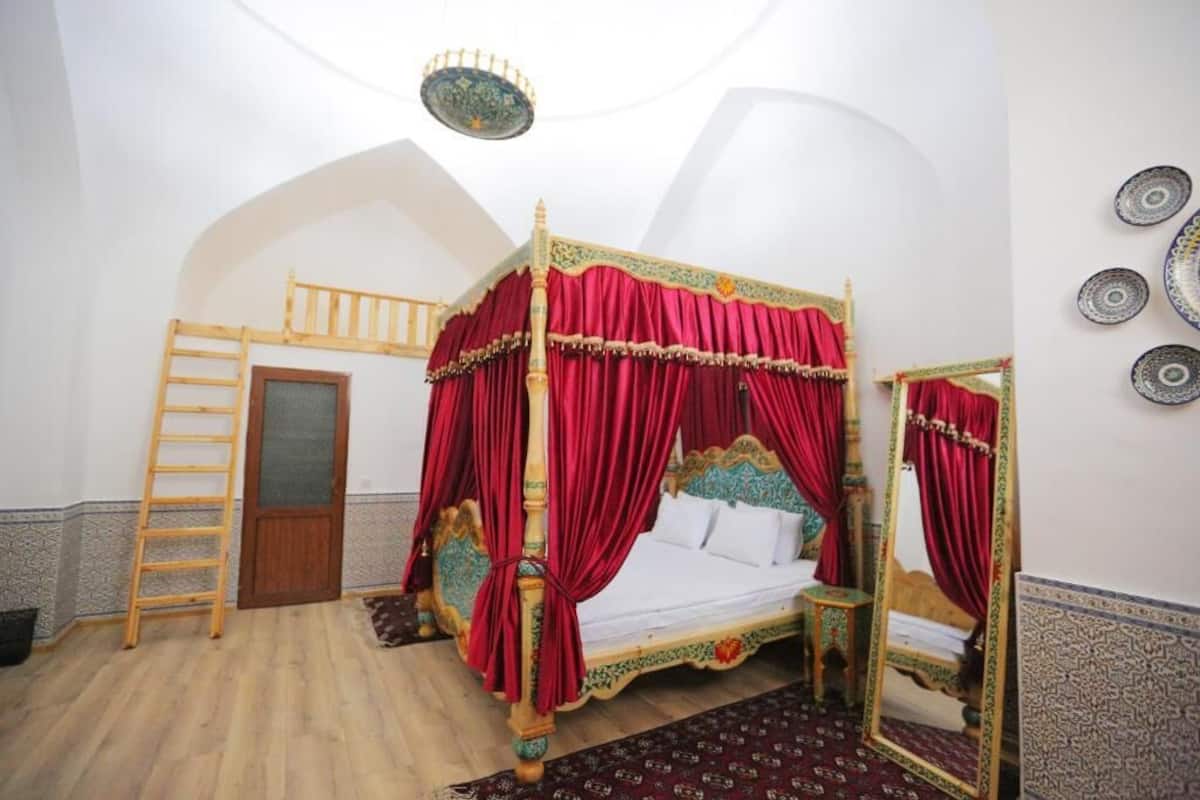 Uma cama de dossel com cortinas vermelhas, uma escada de madeira e um espelho na parede.