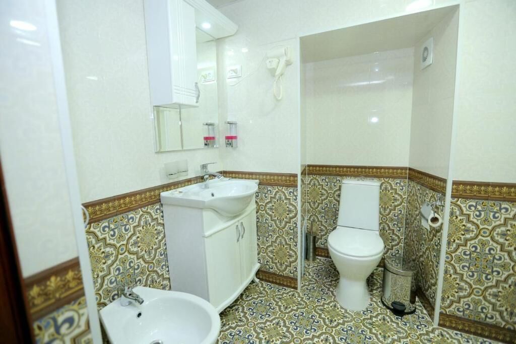Une salle de bain avec un lavabo, des toilettes et un miroir, tous de couleur blanche. Le sol est recouvert de carreaux à motifs, et il y a une poubelle près des toilettes.