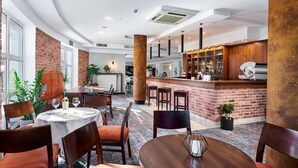 A modern dining area with round tables, brick accents, and a bar area with stools. - Hotel Anton (Pruszków)