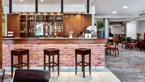 A bar area with a brick counter, stools, and a wooden shelving unit displaying bottles and glasses. - Hotel Anton (Pruszków)