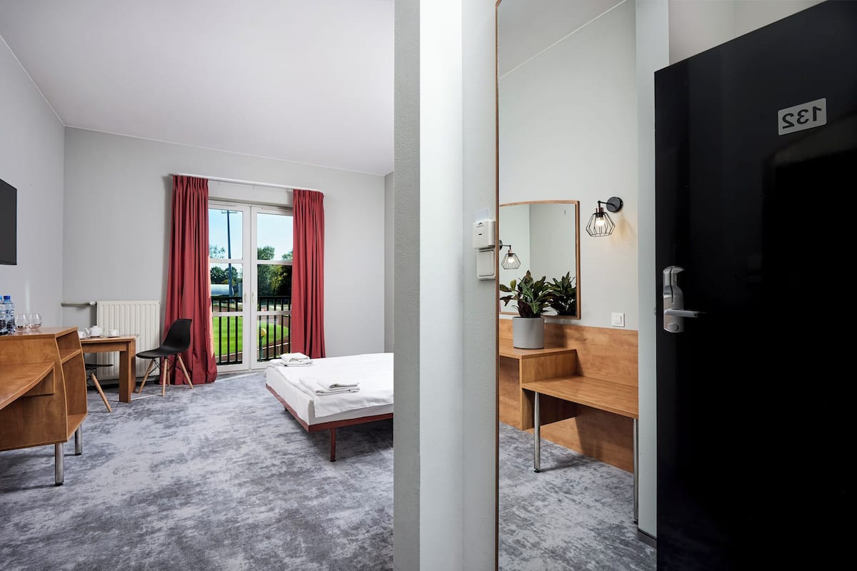 Habitación de hotel con cama, escritorio, silla y baño con espejo, además de una puerta con un letrero.