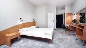 A modern bedroom with a wooden bed, a nightstand, a desk with a chair, and a large mirror. - Hotel Anton (Pruszków)