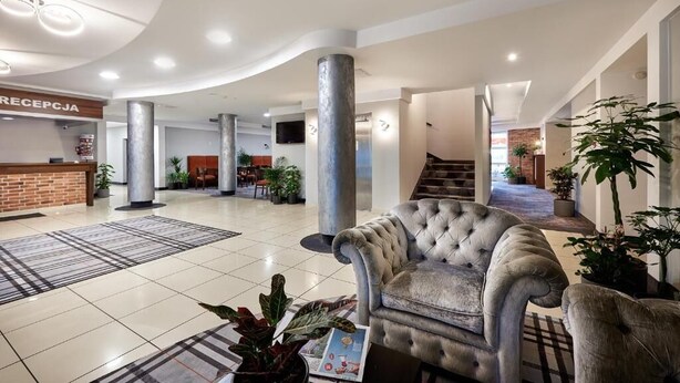 A spacious lobby with a reception desk, a grand staircase, and a plush armchair. - Hotel Anton (Pruszków)