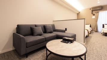 Een moderne hotelkamer met een grijze modulaire bank, een ronde salontafel en een bed met veel kussens.