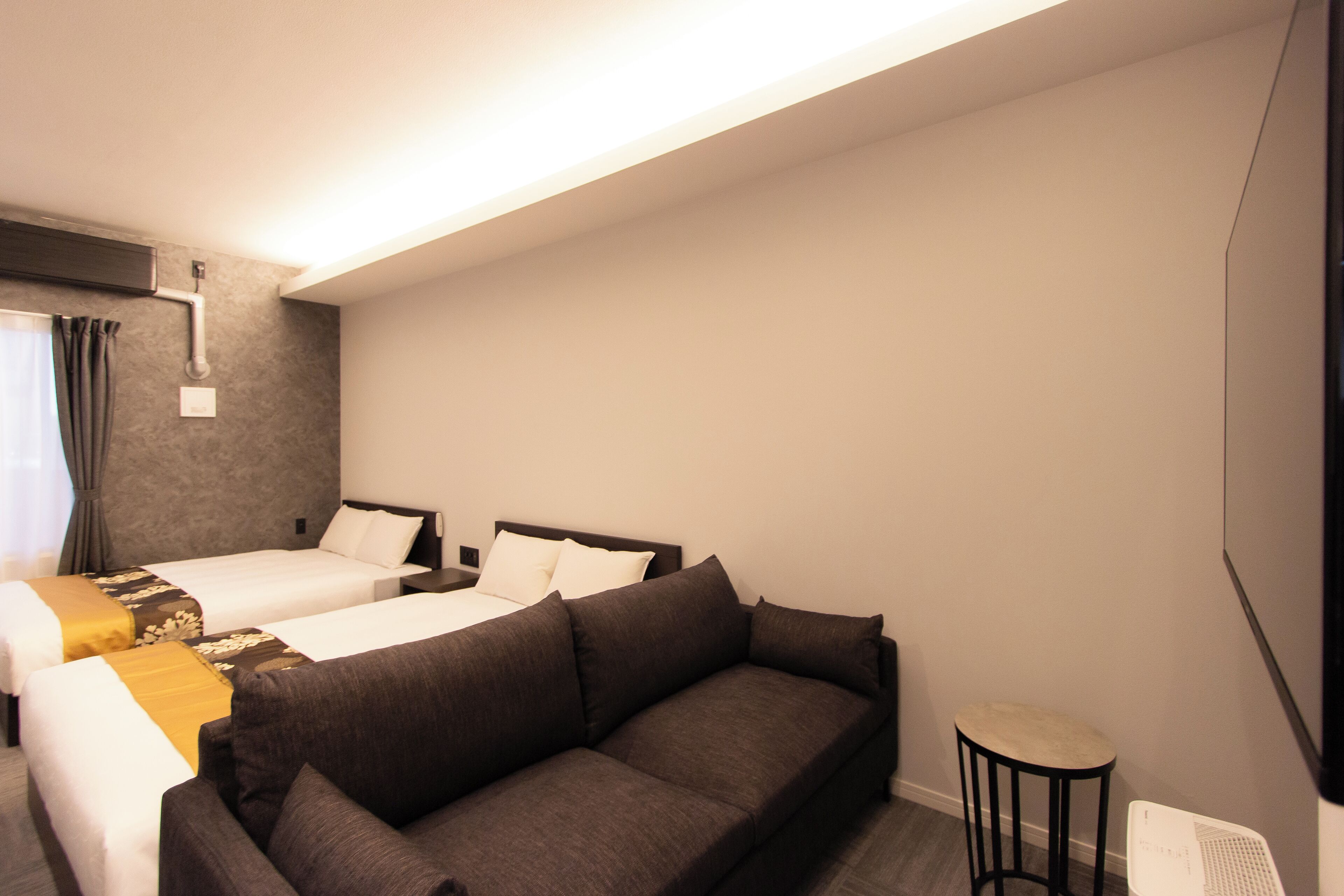 A hotel room with two beds, a sofa, a small table, and a TV.