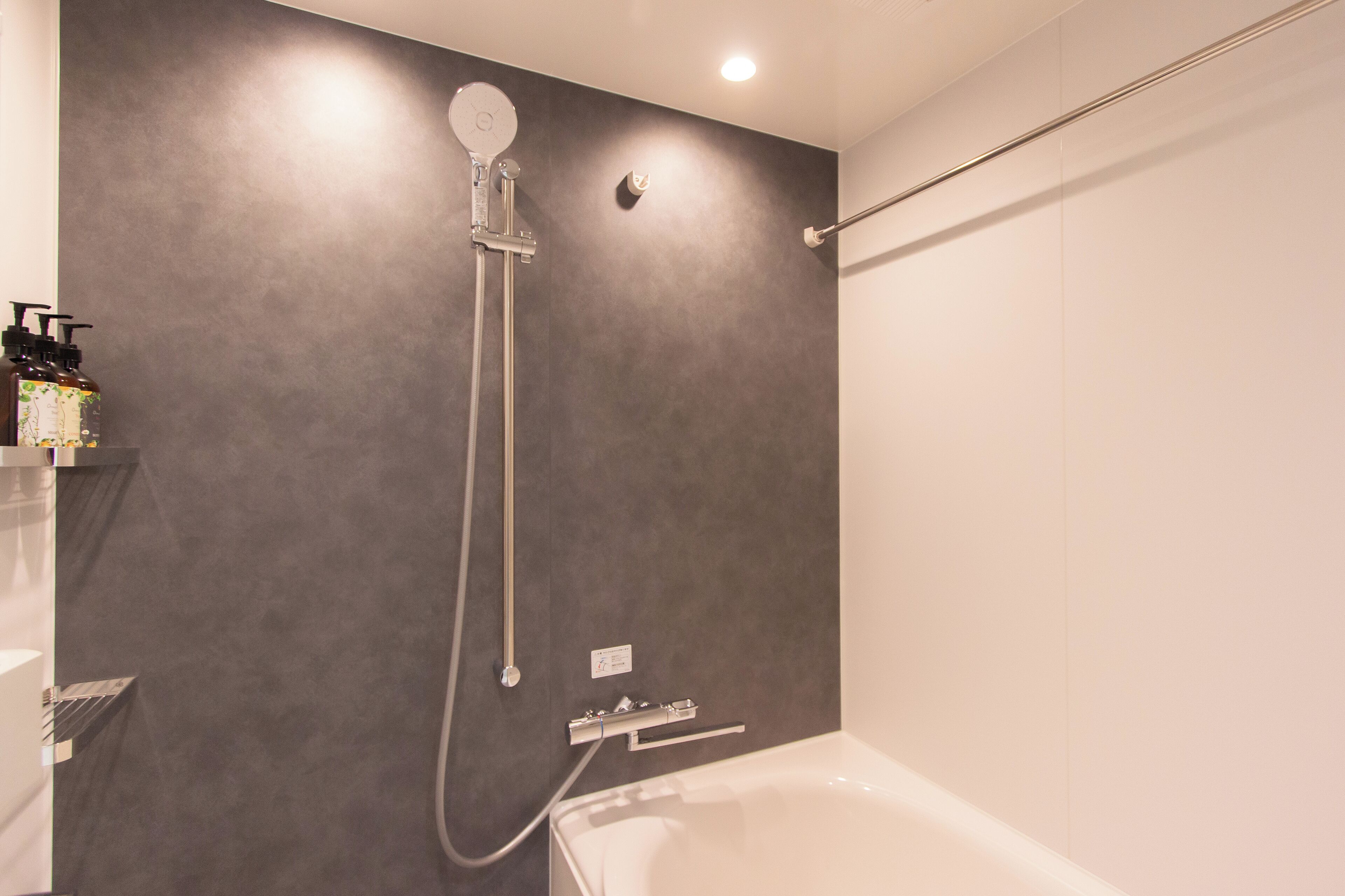 Une salle de bain moderne avec un mur gris, une douche équipée d’un pommeau de douche à main et une baignoire blanche.