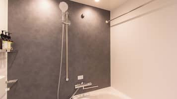 Une salle de bain moderne avec un mur gris, une douche équipée d’un pommeau de douche à main et une baignoire blanche.