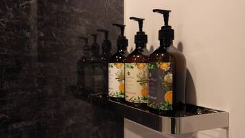 Une salle de bain avec un mur en marbre et une étagère sur laquelle sont posées trois bouteilles de savon liquide pour le corps.