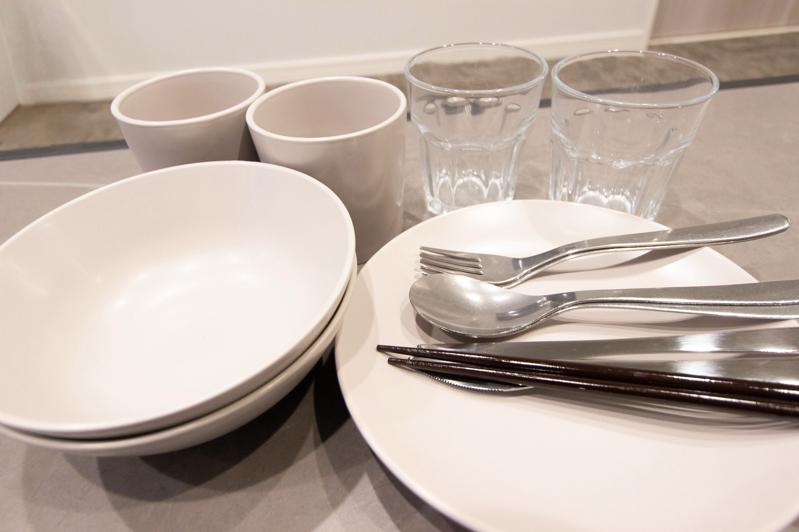 Une table bien dressée, avec une assiette blanche, une fourchette, une cuillère et une paire de baguettes.