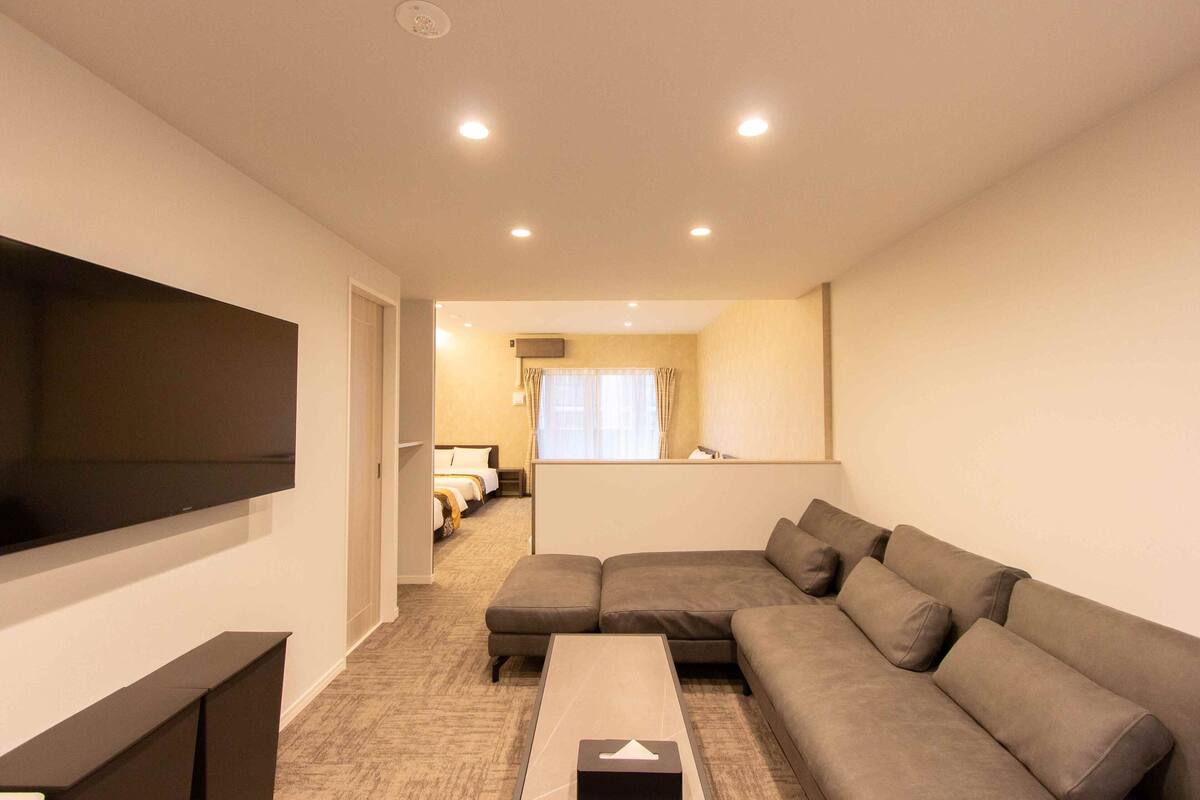 Una sala de estar moderna con un televisor de pantalla plana grande, un sofá seccional y una mesita de centro pequeña.