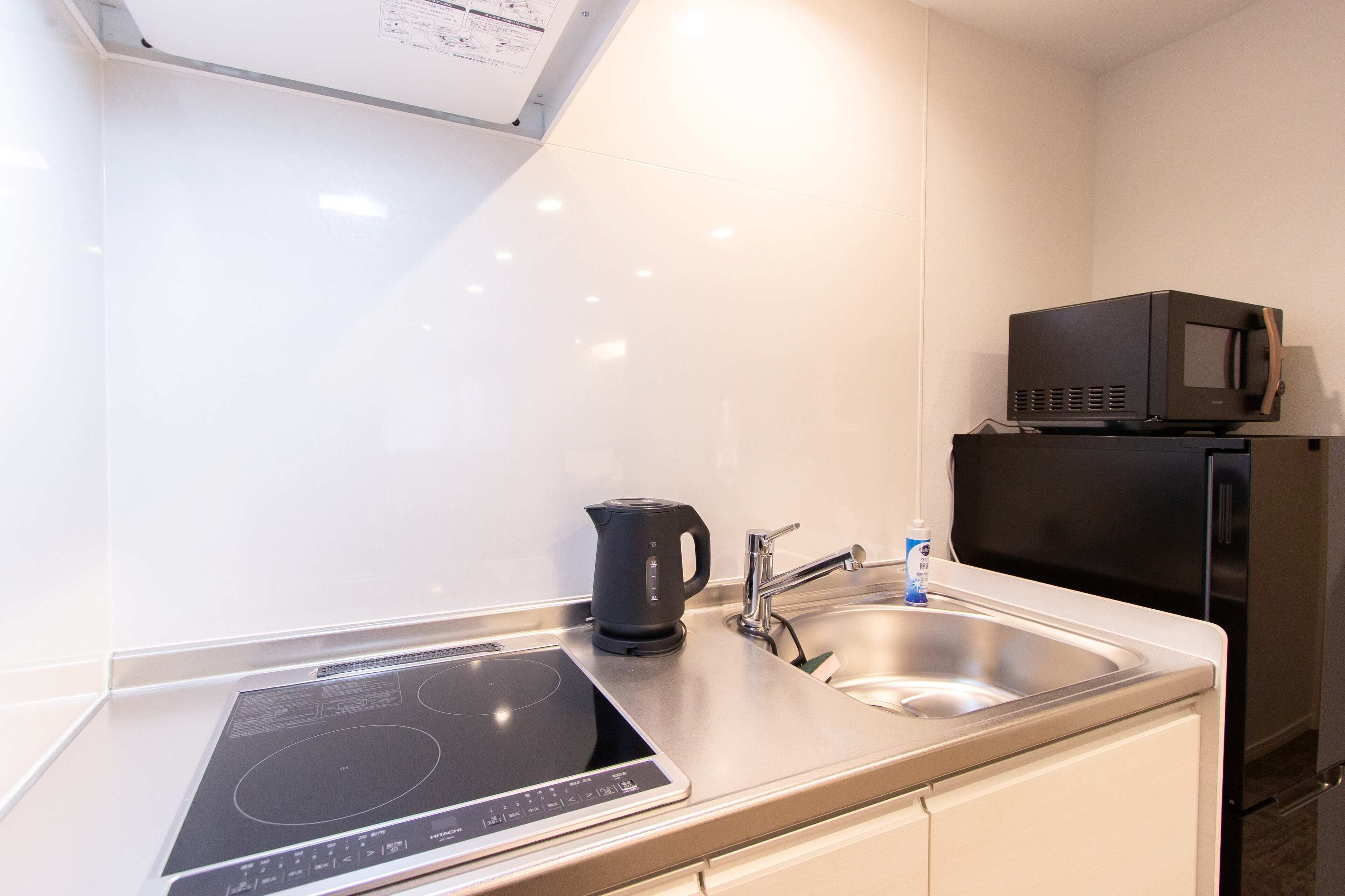 Een moderne keuken met een geïntegreerde inductiekookplaat, een waterkoker, een spoelbak en een magnetron.