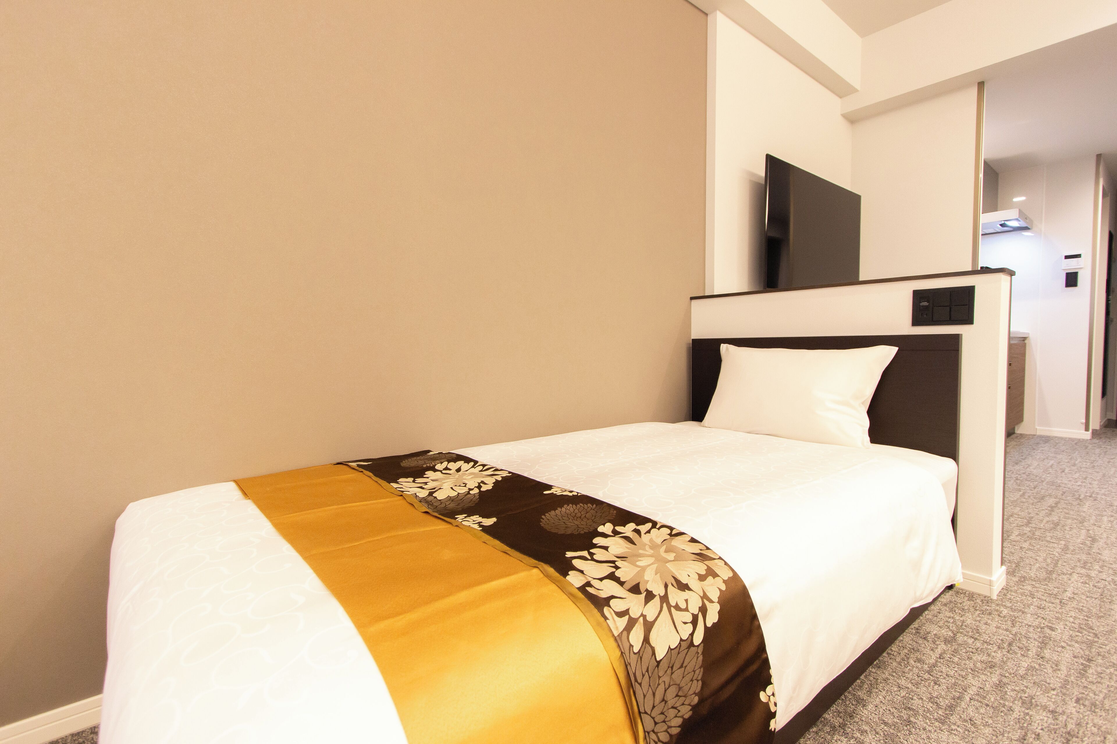 A hotel room with a bed, a television mounted on the wall, and a carpeted floor.