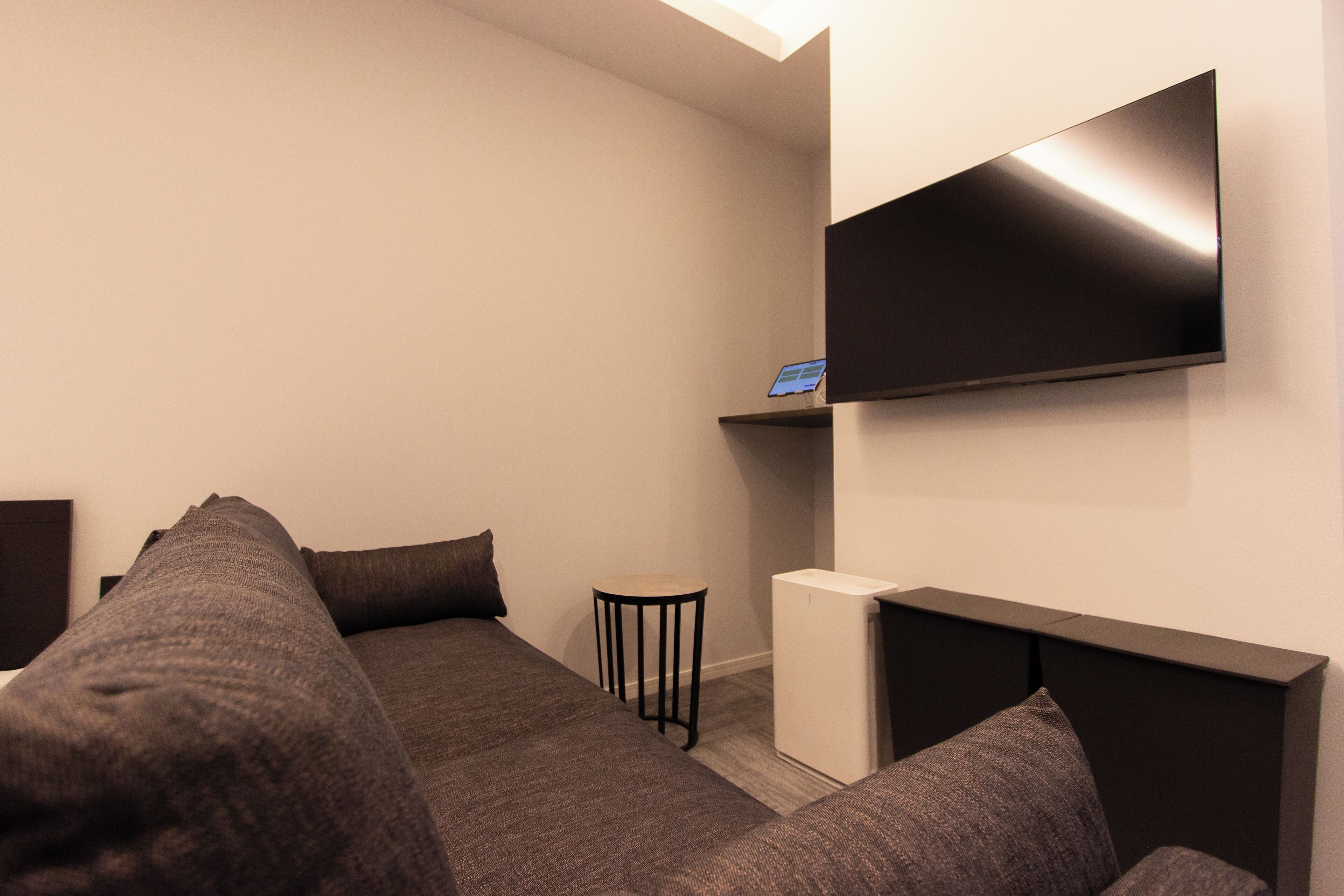 A modern hotel room with a large bed, a small table, a TV mounted on the wall, and a compact white appliance.