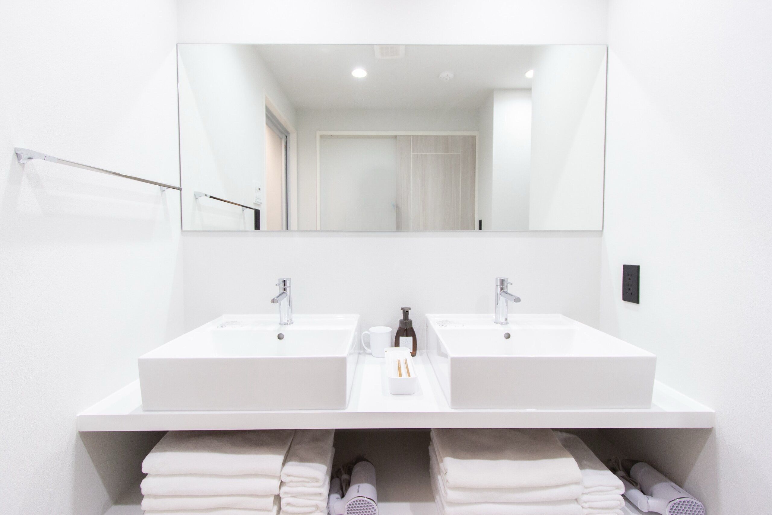 A modern bathroom with two white sinks, a large mirror, and a towel rack.