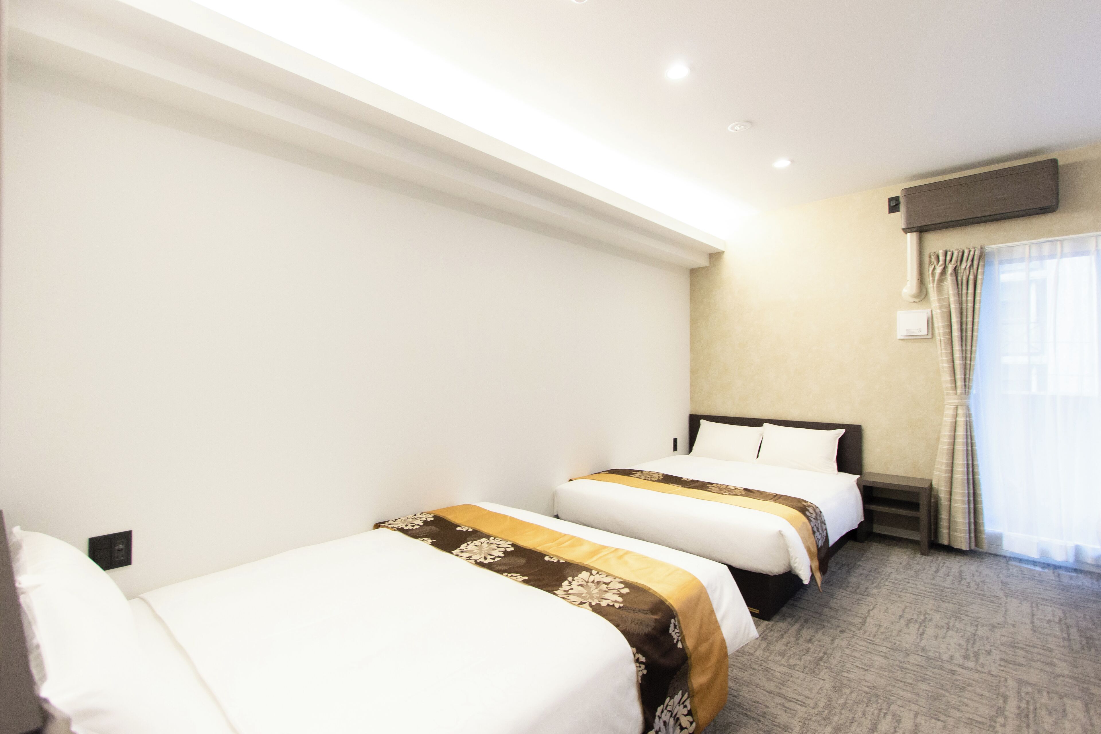 Habitación de hotel con dos camas, un televisor de pantalla plana, una ventana con cortinas y un aire acondicionado instalado en la pared.