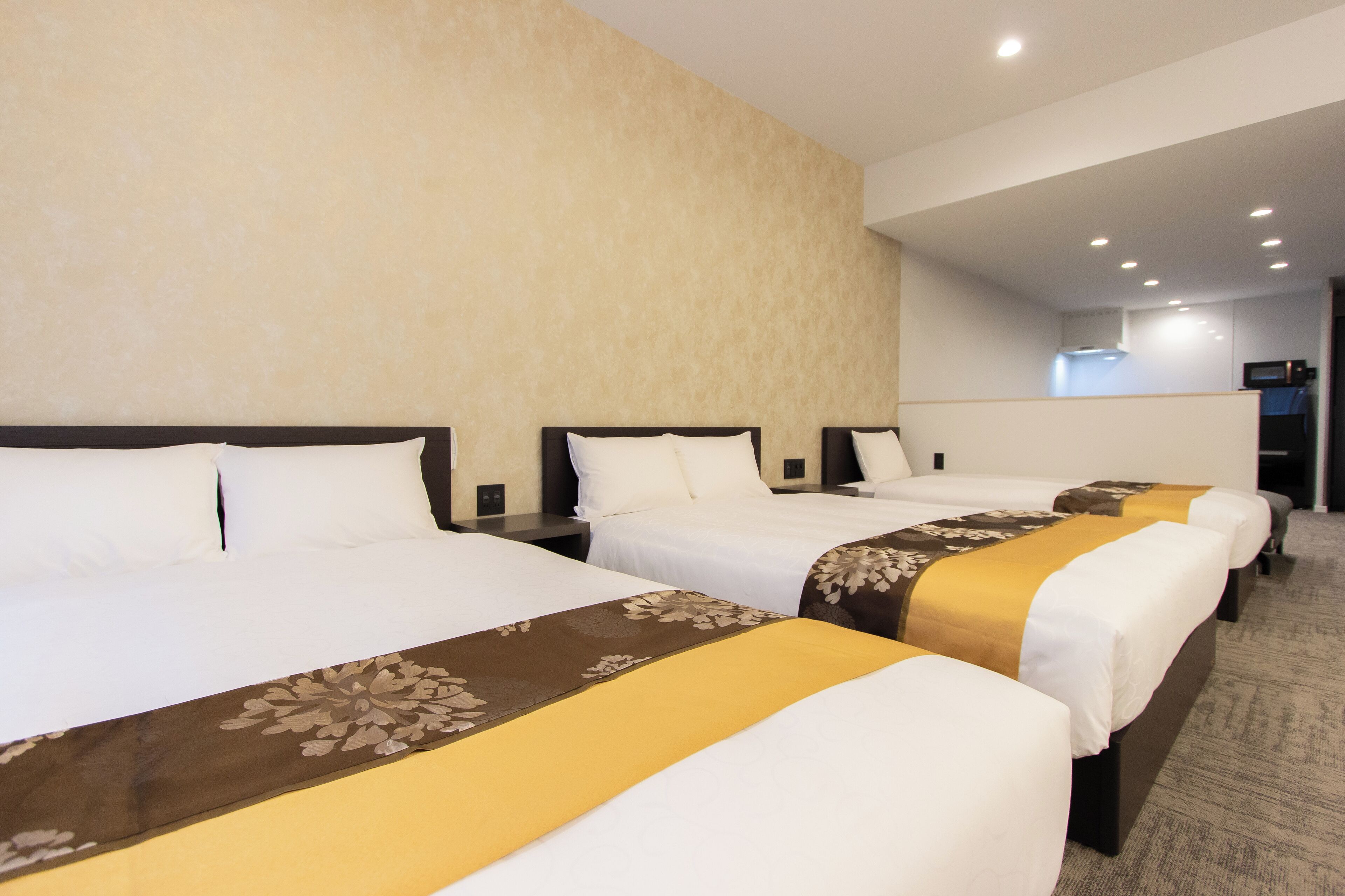 A hotel room with three beds, a kitchenette, and a bathroom.