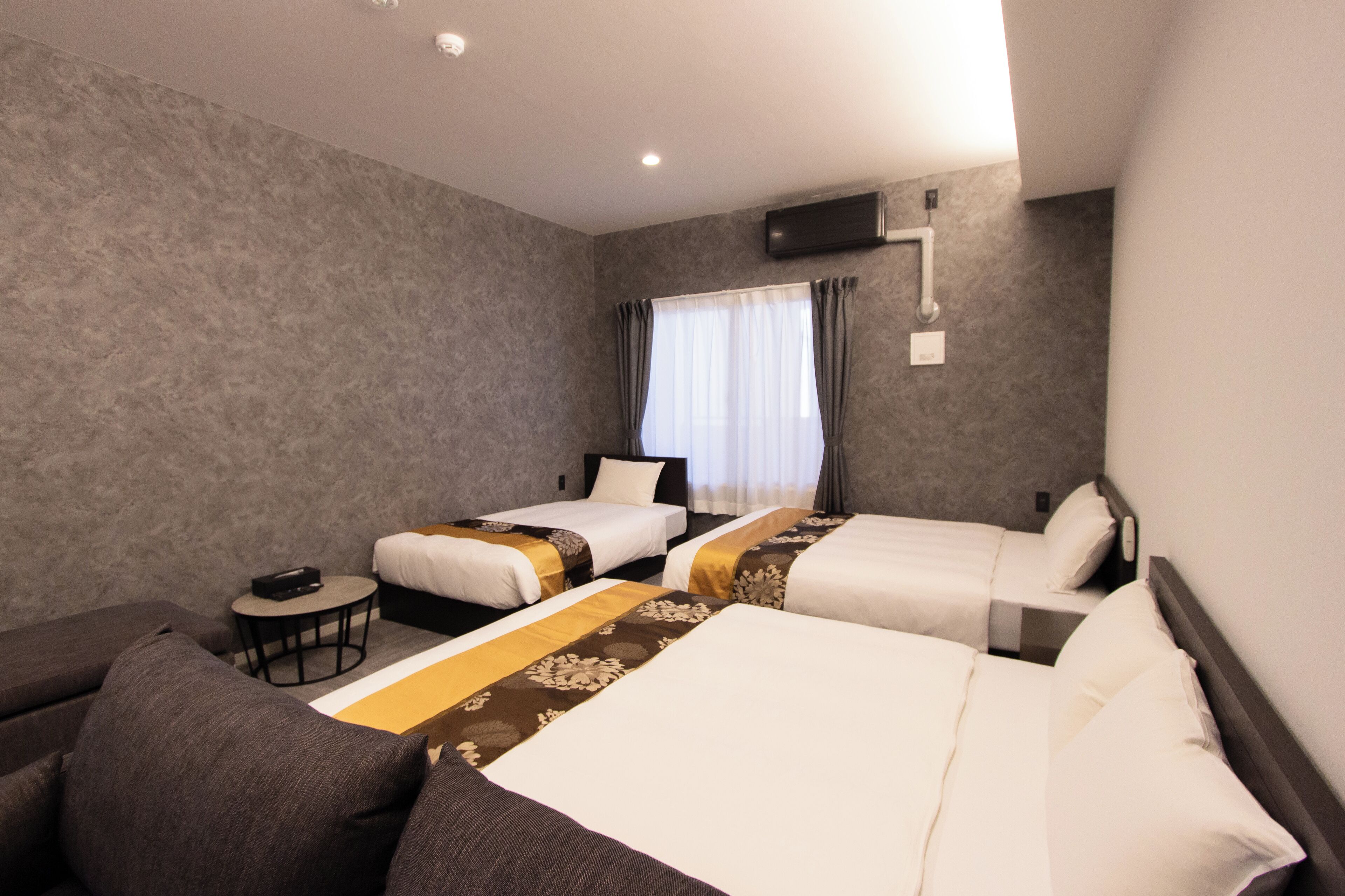 Quarto de hotel com duas camas de solteiro, um sofá, uma mesinha e uma janela com cortinas.