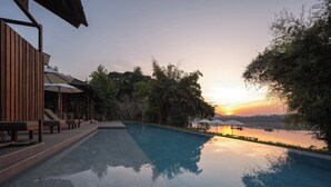 Un área de piscina tranquila con vista al atardecer, mobiliario de cubierta de madera y sombrillas.