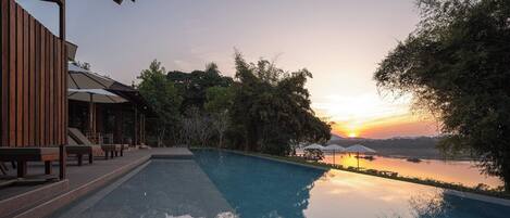 Un área de piscina tranquila con vista al atardecer, mobiliario de cubierta de madera y sombrillas.