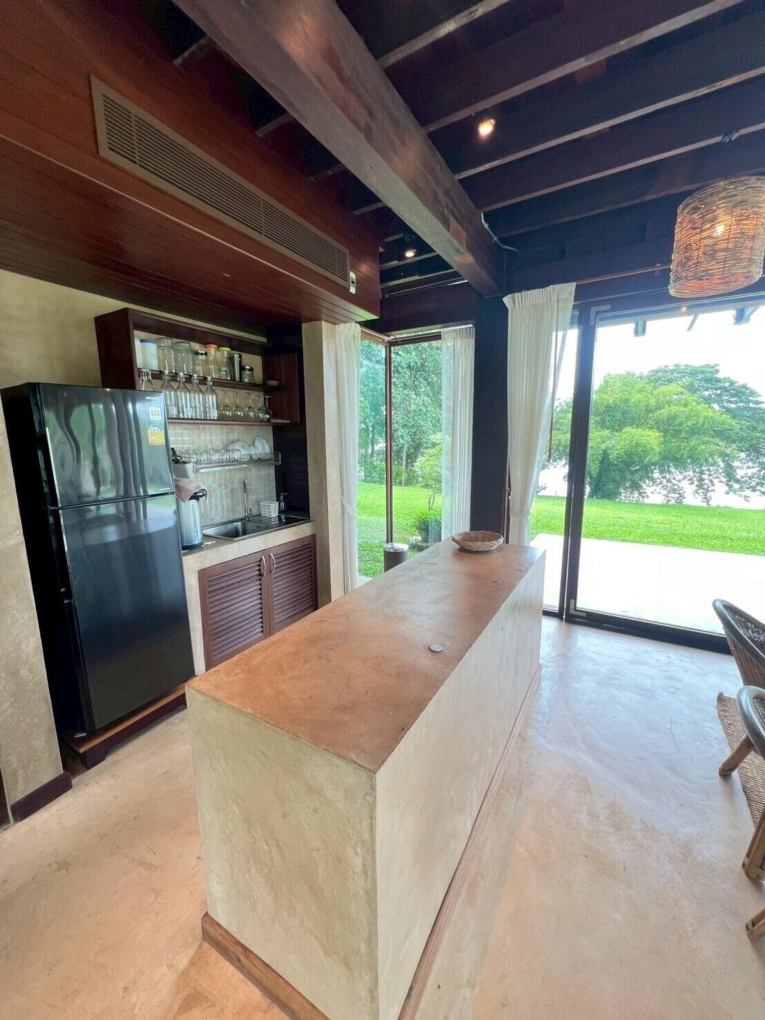 A modern kitchen with a built-in refrigerator, a large island, and a view of a green landscape through large windows.
