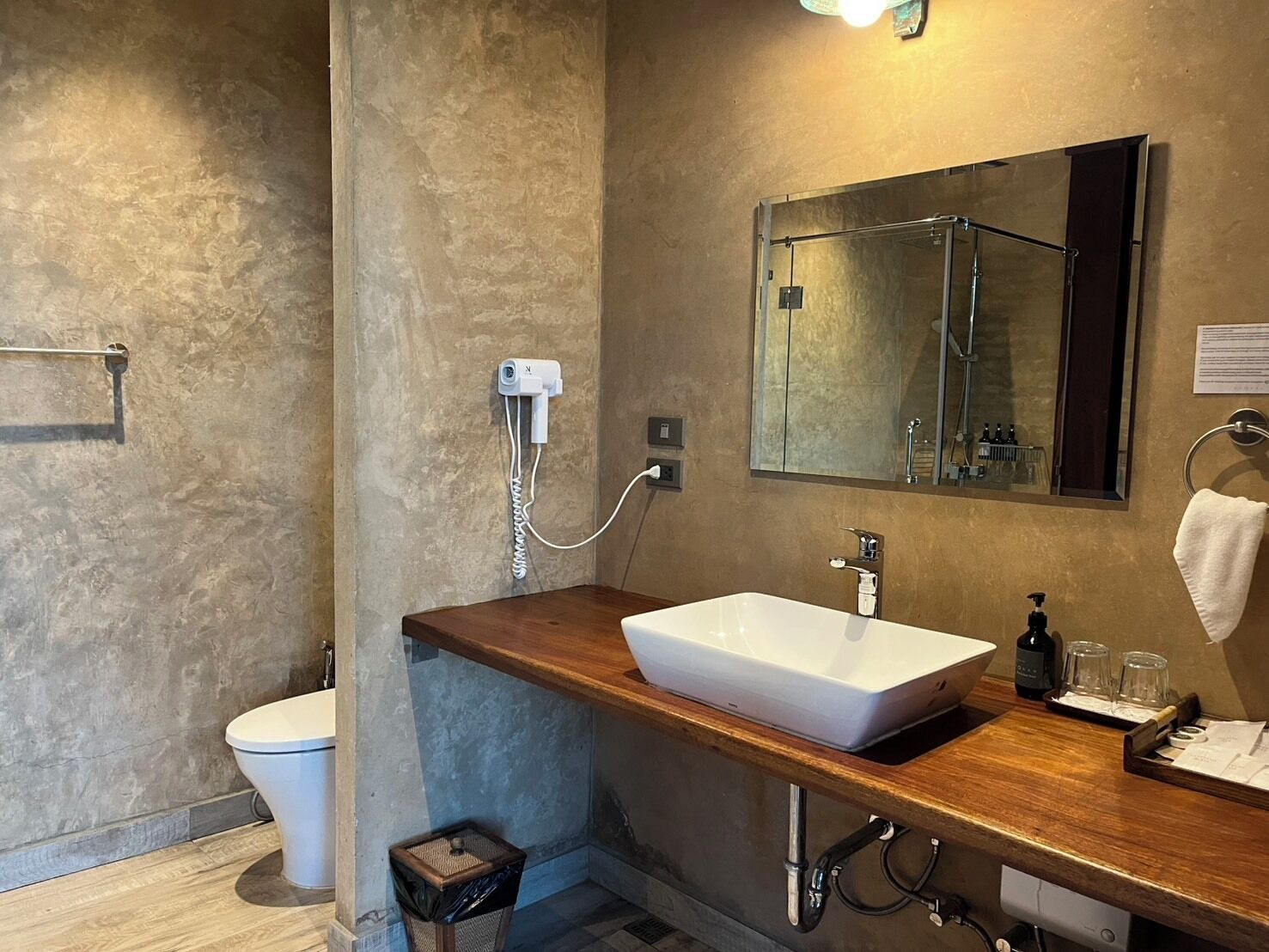 A modern bathroom with a large mirror, a wooden vanity, a white sink, and a shower area.
