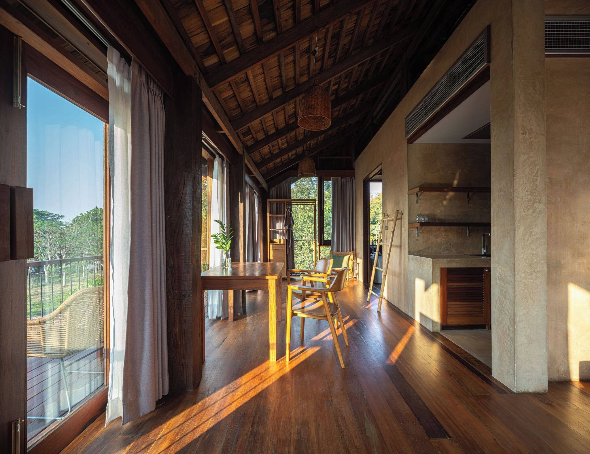 Una habitación amplia con pisos de madera, un comedor con sillas y una mesa, ventanas grandes con cortinas y una cocina con estufa.