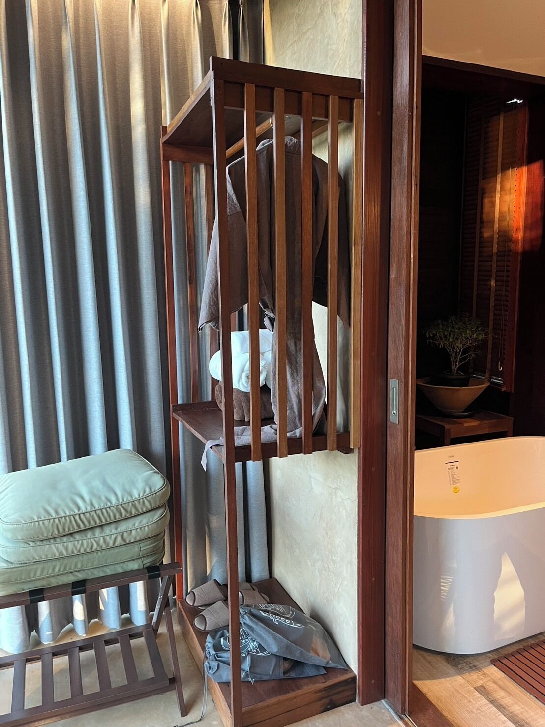 A corner of a room with a wooden crib, a cushioned bench, and a white bathtub.