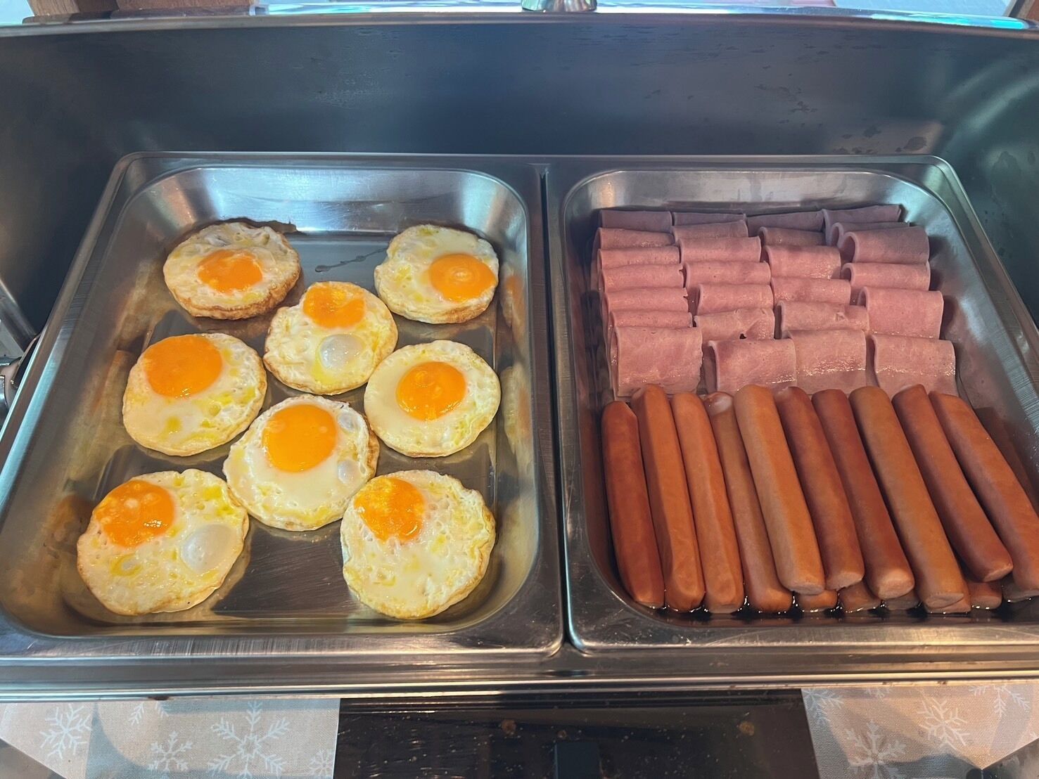 A buffet with two trays: one with eggs and the other with hot dogs.