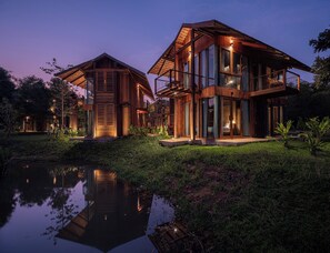 A modern two-story house with large windows and a balcony, surrounded by lush greenery and a pond. - Nachan The Antique Courtyard  (Chiang Khan)