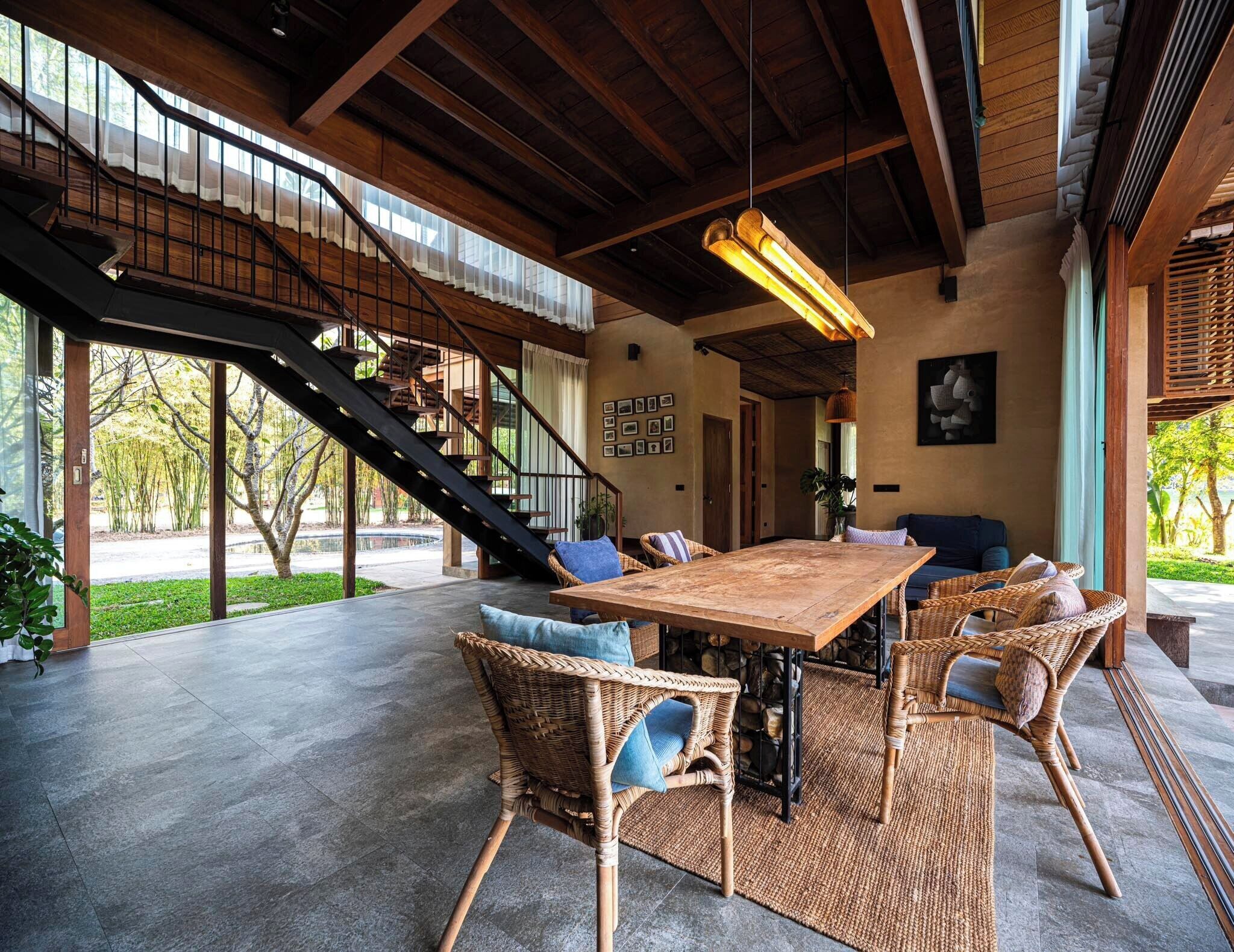 A spacious patio with a large wooden table, wicker chairs, and a staircase leading to an upper level.