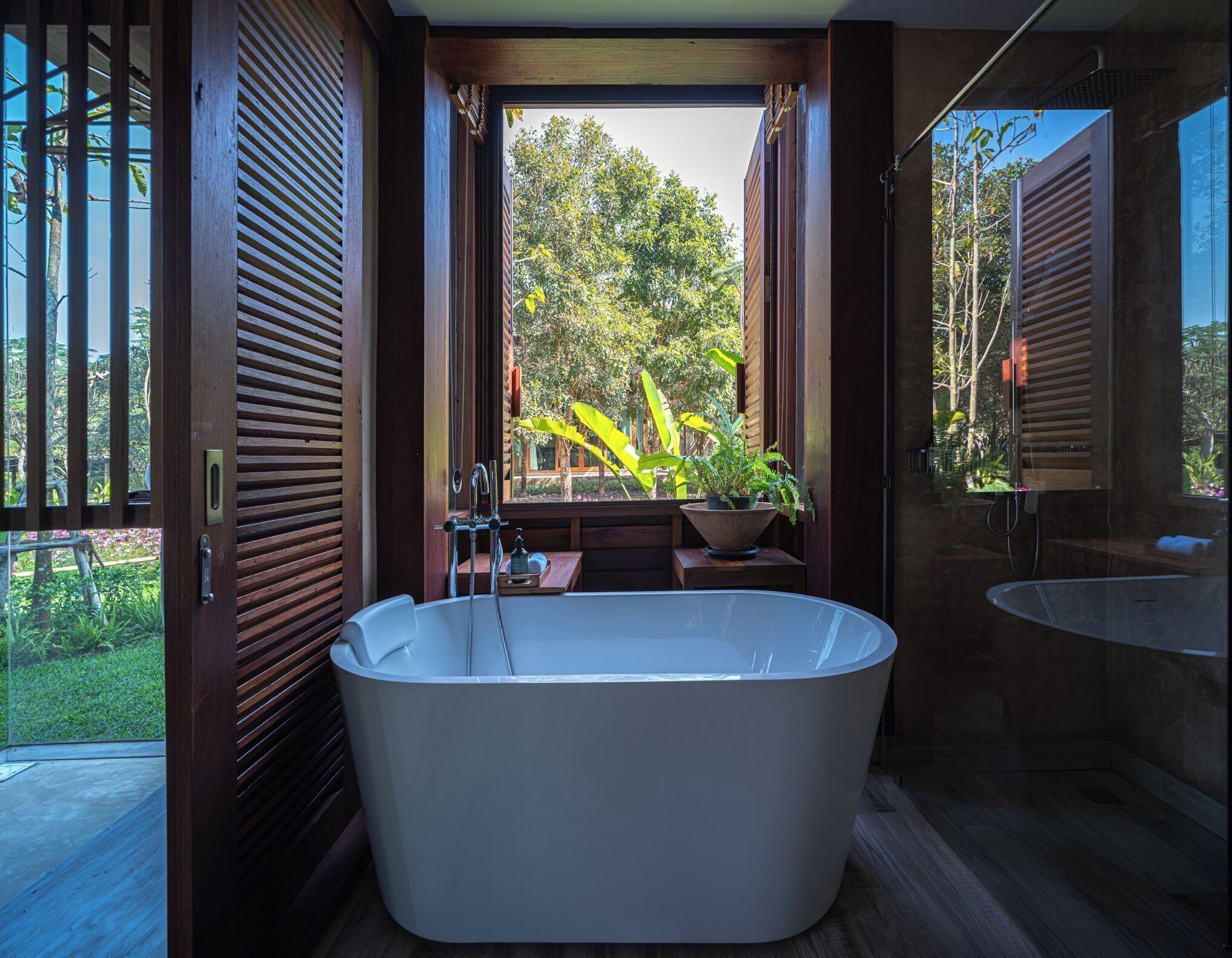 A modern bathroom with a freestanding bathtub, a large window, and a view of a lush garden.