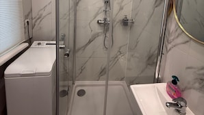 Ett modernt badrum med en duschavdelning med glasväggar, en vit tvättställ och en väggbeklädnad av marmor.