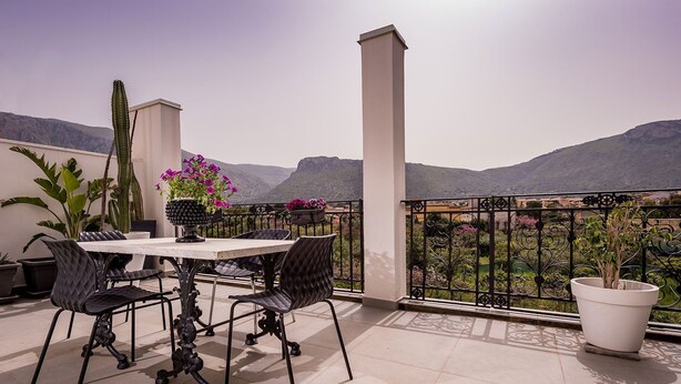 Una terraza con mesa y sillas, plantas en macetas y vistas a montañas.