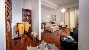 Una sala de estar con sofá, sillones, una mesa de centro, una estantería y un equipo de percusión.