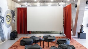Une pièce moderne avec des poufs noirs, un écran blanc et des rideaux rouges.