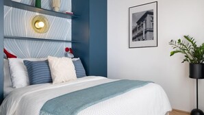 Une chambre à coucher moderne avec un lit, une étagère murale agrémentée d’objets décoratifs, un tableau encadré et une plante en pot.