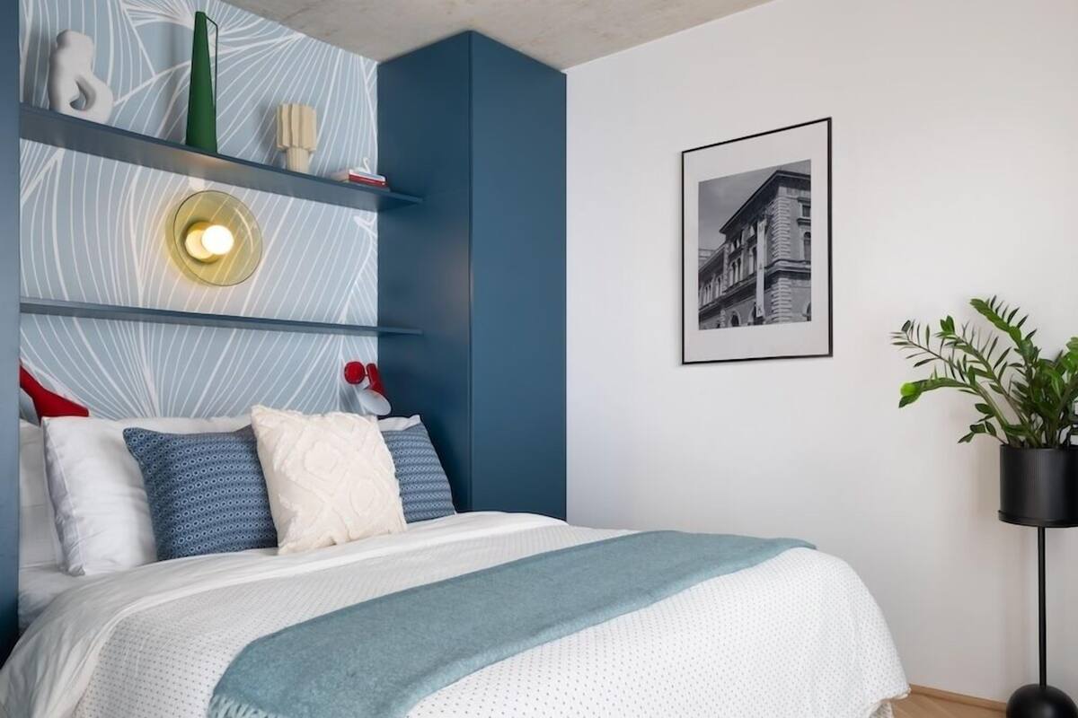 A modern bedroom with a bed, a wall-mounted shelf with decorative items, a framed picture, and a potted plant.