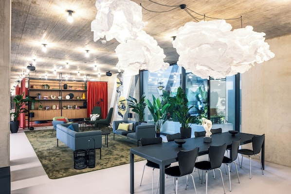 A modern interior with a dining area, sofas, and a large window with a view. - Tribera Vienna Erdberg (Vienna)