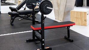 Une salle de sport équipée de matériel de musculation, avec des piliers en béton et un banc en bois.